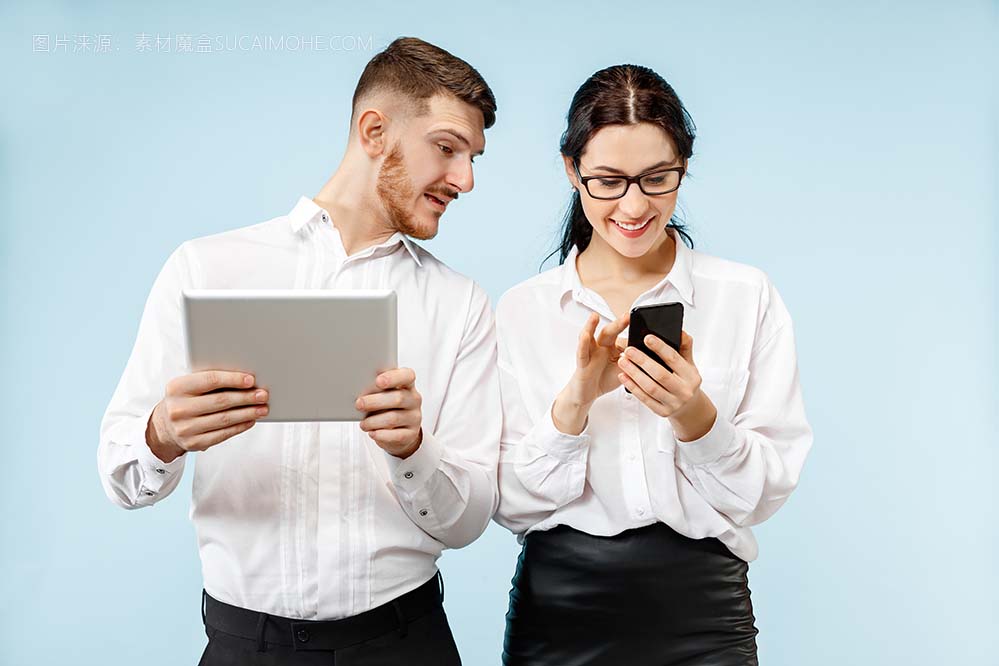 在业务中的伙伴关系的概念。年轻快乐的微笑男人和女人站在工作室的蓝色背景下的手机和平