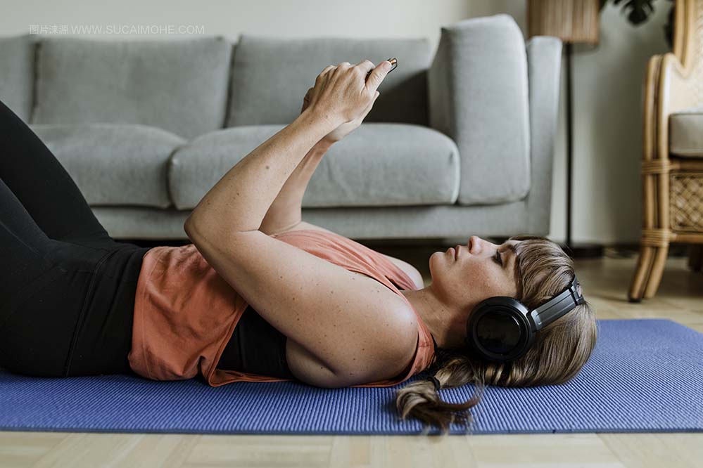 美少女在冠状病毒隔离期间躺在瑜伽垫上时从她的手机选择音乐